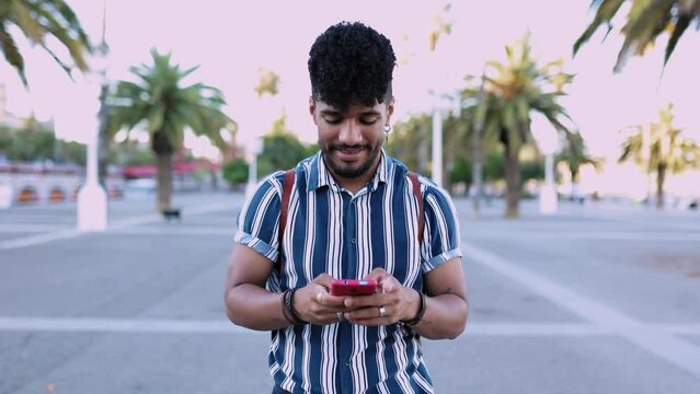 Front view of young trendy hispanic american man using mobile phone while walking outdoor in city street. Slow motion high quality 4k footage