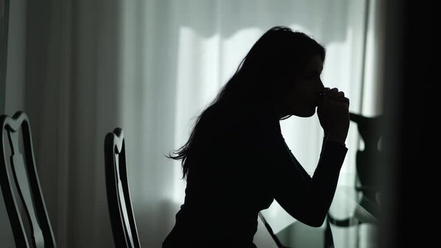 Silhouette of one depressed young woman sitting at home in the dark. Lonely girl suffering alone from mental illness