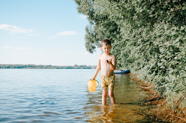 Child playing on lake with bucket and shell. Boy resting in nature during summer holidays.