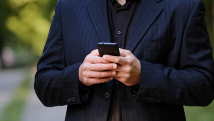 Close up male hands unknown man in black formal suit hold smartphone chatting in social media use mobile app chat texting message search information in internet scroll website page play internet game