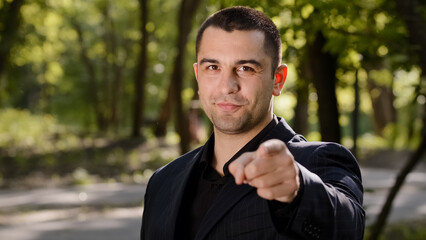 Cheerful confident adult businessman guy show hey you gesture points finger at camera make best choice handsome caucasian man wears formal suit stand outdoors nods head choose option approve good idea