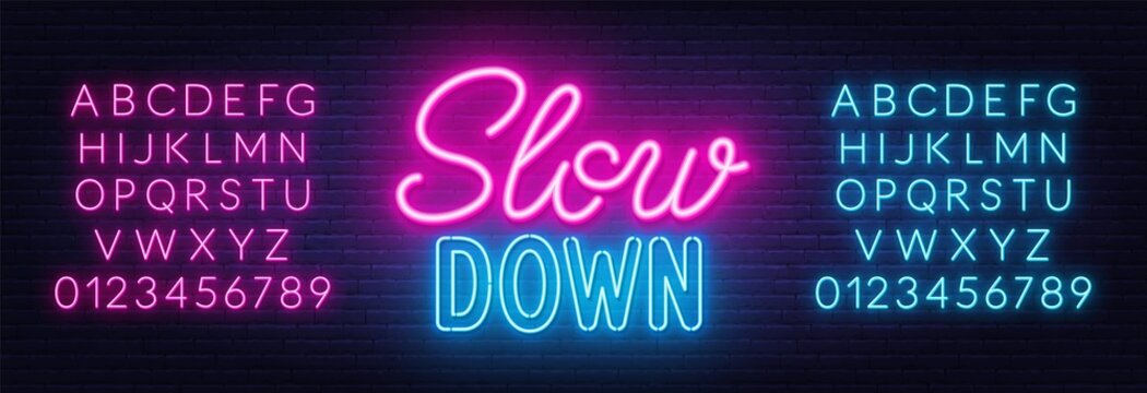 Slow Down neon lettering on brick wall background.