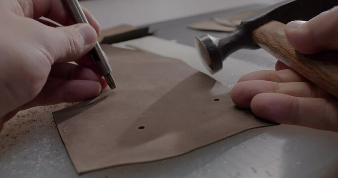 Close up view of master makes holes in leather piece to make shoes in 4k resolution