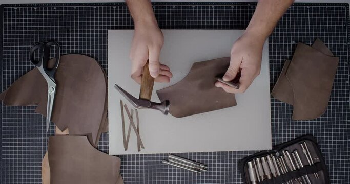 Top view of master makes holes in leather piece to make shoes in 4k resolution