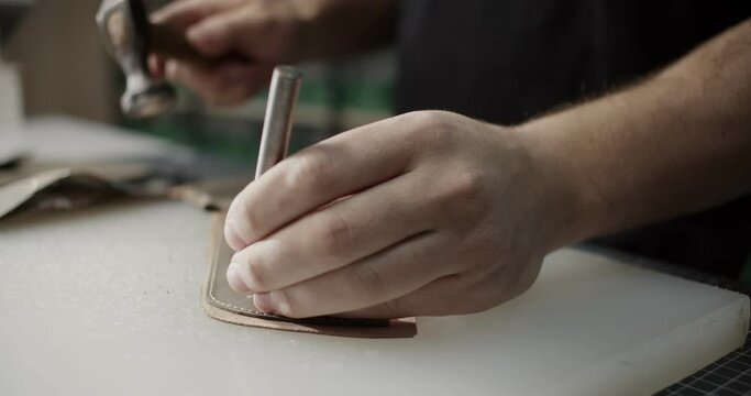 Cinematic close up view of master makes holes in leather piece to make shoes in 4k resolution slowmotion with moving camera focus