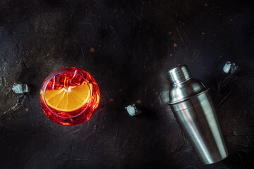 Aperol cocktail with a fresh orange slice and a shaker, Italian summer cold drink, overhead flat lay shot with a place for text, on a black slate background