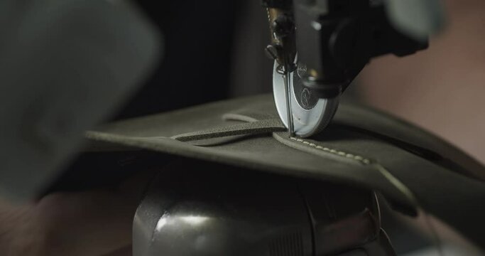 Tailor works on sewing machine in private leather craftshop, making shoes in process. male seamstress sewing leather shoes in leather workshop in 4k