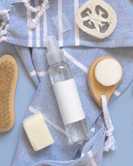 Fototapeta na wymiar Spray bottle on blue bath towel near tropical leaves and skin care accessories, mockup