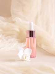 Pink Dropper Bottle near white orchid flower on light yellow close up. Skincare beauty product