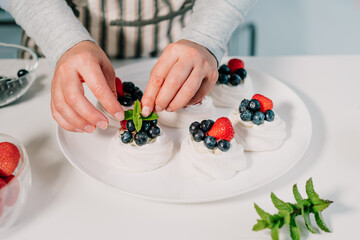 Cooking, making homemade meringue. Female hands decorating pavlova cakes with fresh berries on the kitchen table with ingredients. Recipes for delicious light desserts. Selective focus