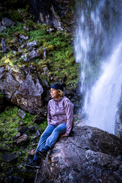 Mature female woman sitting on a wet rock in front of a wild waterfall in northern Sweden.