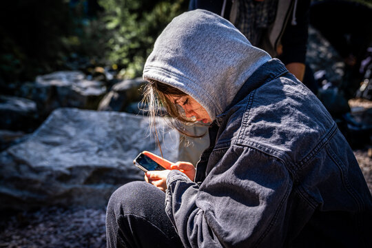 Side view of young female sitting down holding a mobile phone. Focused on phone in nature surroundings.