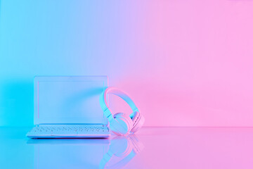 Office table with notebook computer and headphones in vibrant gradient holographic neon colors with copy space. Concept art. Minimal office surrealism.