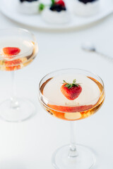 Cocktail drinks with fresh strawberry and meringue Pavlova cakes with fresh strawberries and blueberries on the white plate on the background. Desserts and drink for summer party. Selective focus.