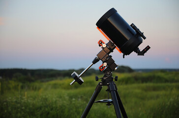 A large amateur optical astronomical telescope points to the sky. Catadioptric telescope on tripod ready for stargazing