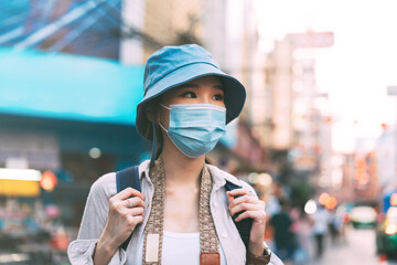 Walking young adult asian woman traveller wear face mask for covid-19 traveling in local city on summer day