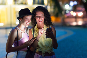Girls using smart phones and talking while out in town at summer night