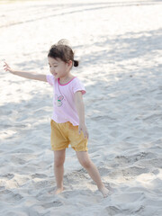 Positive charming 4 years old cute baby Asian girl, little preschooler child playing on sand beach on beautiful sunny day in summer time.