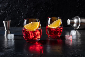 Campari cocktail with fresh oranges, a jigger, a shaker, and ice cubes, on a dark background with copy space