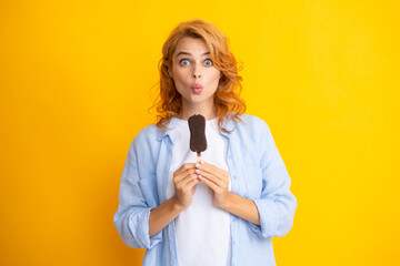 Portrait of beautiful woman eating ice cream on orange yellow background. Girl eating popsicle ice pop. Happy excited expression female portrait. Amazed surprised woman face.