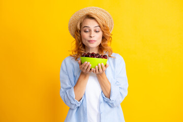 Attractive young woman eating fresh cherry. Healthy summer fruits. Yellow background. Beautiful woman posing with a cherry, girl with cherry promoting.