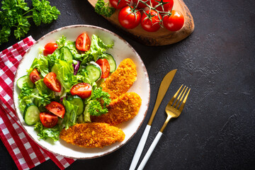 Chicken nuggets with fresh salad at dark stone table. Top view image.