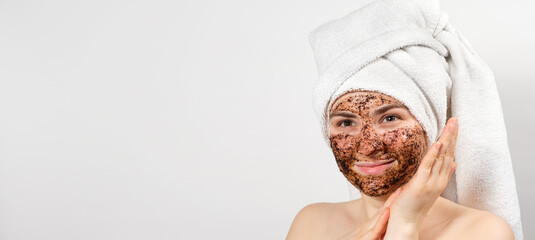 A beautiful young woman with a bath towel on her head and a coffee mask on her face takes care of...