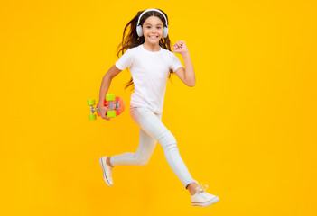 Fototapeta na wymiar Jump and run. Teenagers youth casual culture. Teen girl with skateboard and headphones over isolated studio background. Teenager in fashion stylish clothes. Smiling girl.
