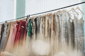 Beautiful dresses with embroidery, beads and sequins hang on hangers in a luxury clothing store.