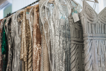 Beautiful dresses with embroidery, beads and sequins hang on hangers in a luxury clothing store.