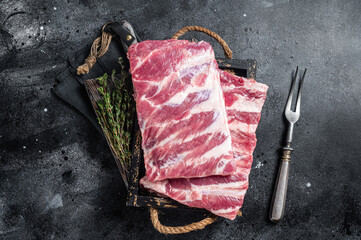 Fresh rack of raw pork spare ribs with herbs. Black background. Top view