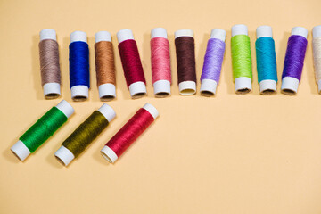 A set of multi-colored threads for sewing with an empty space for text on a beige background, top view. Tailoring and needlework equipment, tailor banner.