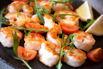 Roasted shrimps with tomatoes and arugola on black plate