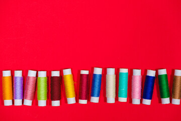Fototapeta premium A set of multi-colored threads for sewing with an empty space for text on a red background, top view. Tailoring and needlework equipment, tailor banner.