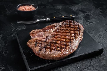 Gordijnen Grilled top sirloin or rump steak on a marble board. Black background. Top view © Vladimir