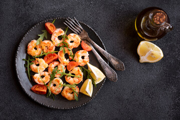 Roasted shrimps with tomatoes and arugola on black plate