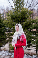 Portrait of a girl in a white scarf and a red dress near a spruce tree in spring