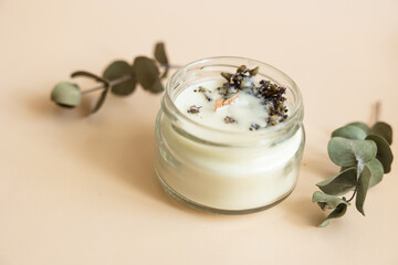 Handmade candle from paraffin and soy wax in glass with wooden wick and dry herbal isolated on pastel beige background. Flat lay, top view, copy space