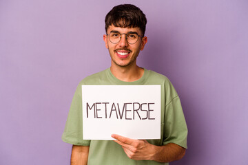 Young hispanic man holding meta verse placard isolated on purple background happy, smiling and...