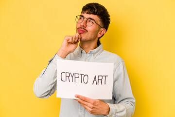 Young hispanic man holding crypto art placard isolated on yellow background looking sideways with doubtful and skeptical expression.