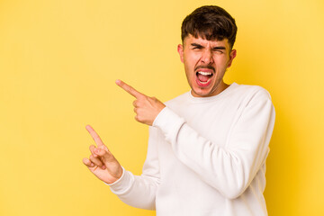 Young caucasian man isolated on yellow background pointing with forefingers to a copy space, expressing excitement and desire.