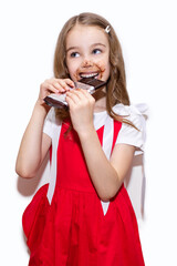 A little girl eats a bar of chocolate on a white vertical background. Happy child with face and hands covered in chocolate. The concept of children's happiness and love for sweets