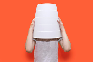 The child put a bucket on his head while sitting on an orange background. Funny child hid in a...