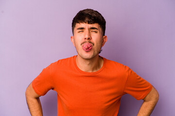 Young caucasian man isolated on purple background funny and friendly sticking out tongue.