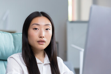 Portrait of a young Asian woman in the office, close-up photo of a long-haired business woman looking at the camera.