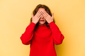 Young caucasian woman isolated on yellow background afraid covering eyes with hands.