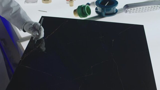 Construction laboratory testing the quality of porcelain tile or stone by Scratch Pin Probe . Worker of laboratory scratching tile by scratch tester pen . Close up view of hands .  Slow motion