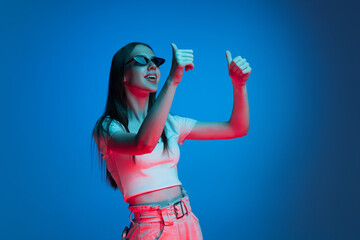Half-length shot of emotional girl with long glossy dark hair isolated on blue background in neon light. Concept of beauty, art, fashion, emotions