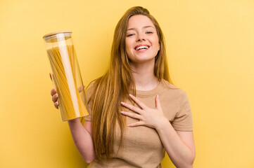 Young caucasian woman holding a spaghettis jar isolated on yellow background laughs out loudly keeping hand on chest.