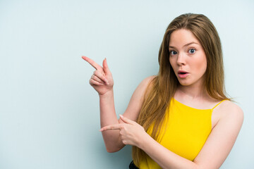 Young caucasian woman isolated on blue background pointing with forefingers to a copy space,...